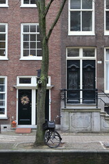 Fototapeta na wymiar Amsterdam Canal Street View Close Up with House Entrance, Christmas Wreath, Tree and Parked Bicycle, Netherlands