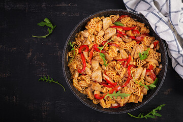 Heart-shaped pasta  in tomato sauce with chicken and sweet pepper with arugula on a dark table. Top view