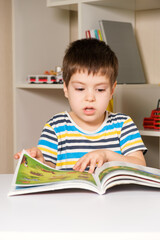 A boy in a striped T-shirt reads a book, flips through pages with pictures