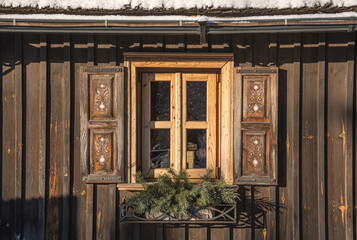 Old wooden window with roof covered by snow with fir branches and decorations 