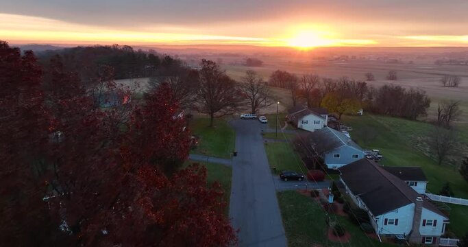 Aerial flight establishing shot of homes along street in USA. American homes at colorful sunrise. Quiet autumn winter scene in rural countryside.