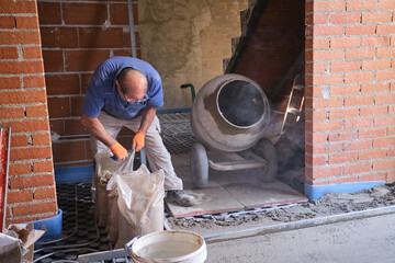 Construction worker opening sandbags to loads a concrete mixer.