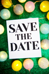 Save The Date text on paper card with LED cotton balls decoration on green background