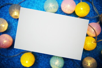Empty paper card mockup and LED cotton balls decoration on blue bokeh background