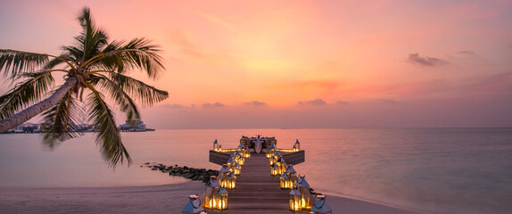 Romantic dinner on the beach with sunset, candles with palm leaves and sunset sky and sea. Amazing view, honeymoon or anniversary dinner landscape. Exotic island evening horizon, romance for a couple
