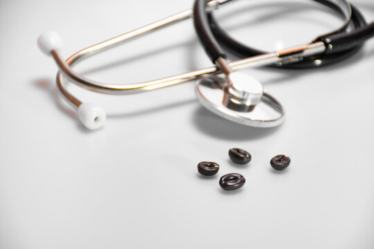 Four roasted coffee beans on a white background next to a stethoscope or phonendoscope: a place for text, high blood pressure, hypertension or hypotension and pulse diagnosis, medical concept