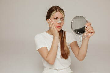 A young woman with a bandage on her nose after rhinoplasty with a mirror in her hand