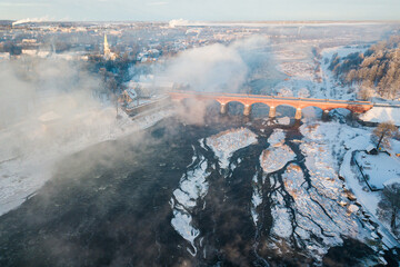 River Venta and long brick bridge in foggy winter day, Kuldiga, Latvia. Captured from above