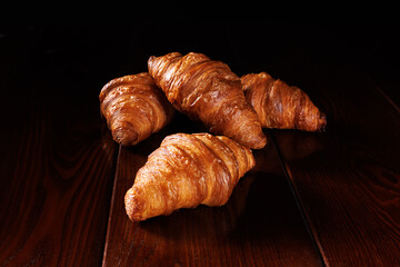 Several croissants lie on a dark varnished table.