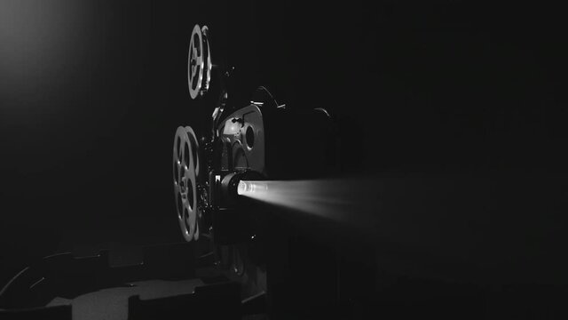 Monochrome shot of an old-fashioned antique 8mm film projector projecting a beam of light in a dark room. The camera flies around