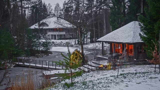 Day To Night Timelapse Of A Winter Village With Unrecognizable People Gathering Around A Fireplace In The Snowy Exterior