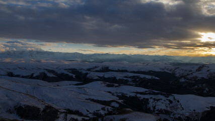 The setting sun illuminates the mountain range through the clouds