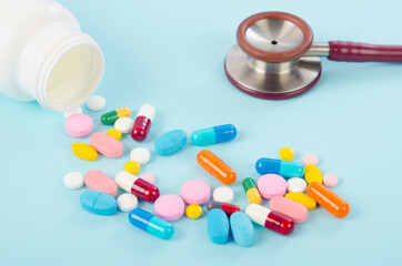Medical pills and tablets spilling out of a drug bottle on blue background.