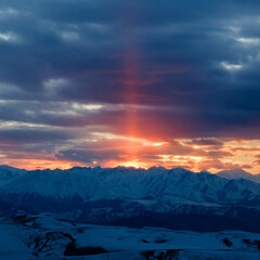 Fototapeta na wymiar The setting sun illuminates the mountain range through the clouds