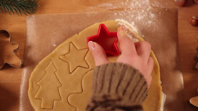 Woman making gingerbread at home. Female cutting cookies of gingerbread dough, view from above. Top view of woman using making gingerbrean star-shaped
