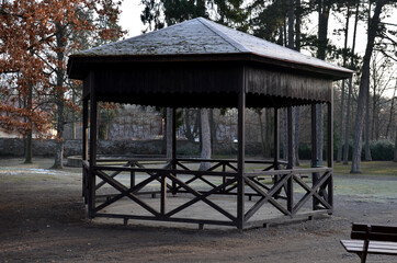 Fototapeta na wymiar polygonal pergola with benches and a fence around the perimeter. there is a lot of space inside. the roof is pyramidal covered with asphalt shingles, in natural park, footpath, gravel
