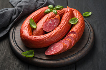 Smoked sausage with fresh basil on a cutting board on a dark background.