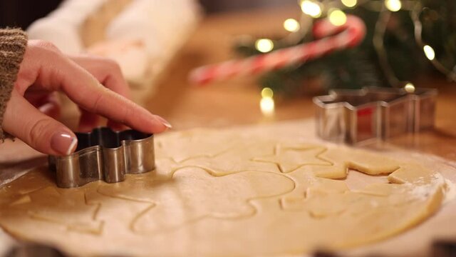 Home bakery, woman cooking traditional festive sweets. Female cutting cookies of raw gingerbread dough on wooden table. New Year celebration traditions. Christmas mood