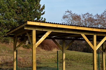 Fototapeta na wymiar cheap wooden pergola in the meadow serves as a shelter for the playground in the housing estate. flat roof, yellow wooden columns with reinforcement