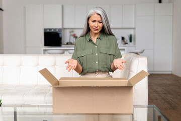 Disappointed middle-aged Asian lady upset with an online purchase. Gray-haired woman looking inside...