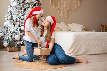 Sisters celebrate winter holidays. Girls exchange Christmas gifts near Christmas tree. Happy among New Year's decor. 