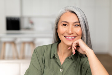 Close-up portrait on senior gray-haired woman in home interior, charming mature asian lady looking...