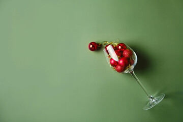 Wine glass filled with red christmas balls on green background.