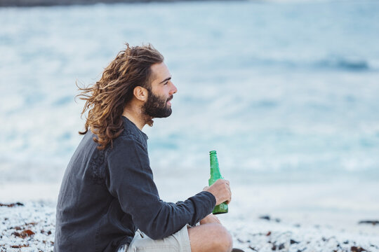 Thoughtful young man with beer bottle at beach - Powered by Adobe