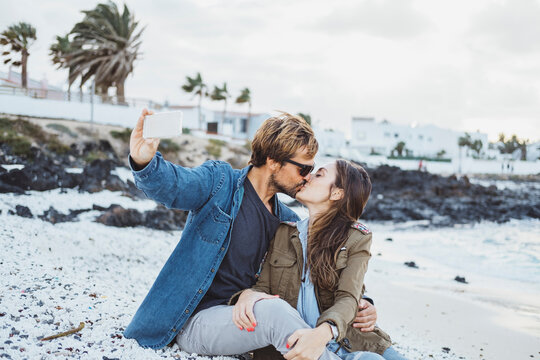 Boyfriend kissing girlfriend while taking selfie through smart phone at beach