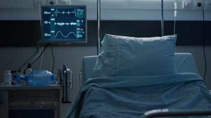 Empty hospital ward prepared for patient healthcare at modern medical facility. Nobody in intensive care room equipped with reanimation technology, monitor, surgery equipment and bed