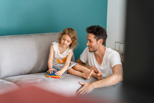 Daughter playing with puzzle while sitting by father in living room