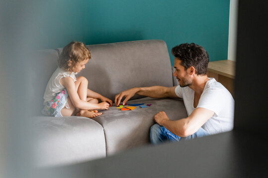 Father helping daughter while playing with puzzle on sofa