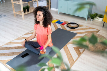 Contemplating woman holding juice jar while sitting on exercise mat in living room