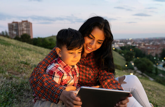 Smiling mother and son using digital tablet while sitting on hill