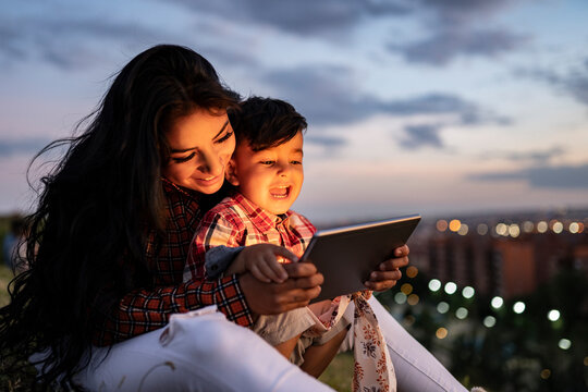Happy son using digital tablet while sitting with mother during sunset