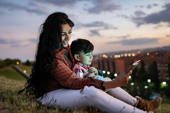 Mother using digital tablet while sitting with son on hill