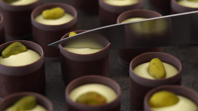Close up of knife cuts milk chocolate candie with creamy filling and pistachio nuts. Food dessert background.