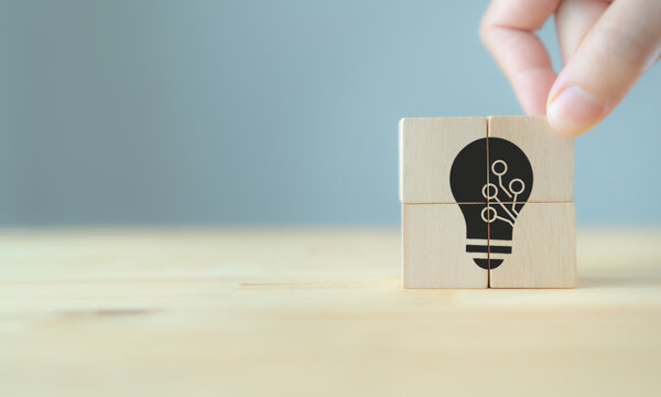 Ideas of innovation and technology concept. High value added product and service for business strategy. Hand puts the wooden cubes; light bulb with technology icon inside. Grey background, copy space.