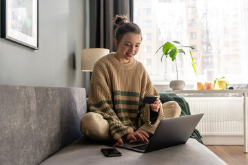 Young woman with credit card doing online shopping on laptop at home