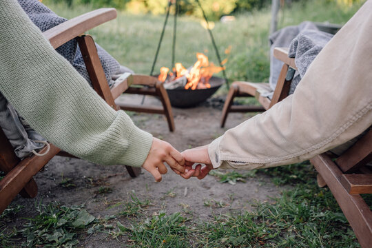 Young couple holding hands while sitting on chair near fire pit