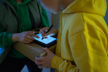 Boy signing on screen with digitized pen while receiving package