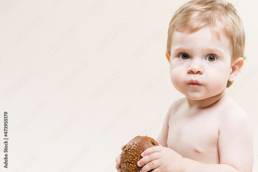 Wall mural natural portrait of little child with food in hands while eating freshly baked bun and posing agains