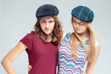 Obraz premium Youth Lifestyle. Two Serious Caucasian Girlfriends Posing Together While Wearing Caps Over White Background.