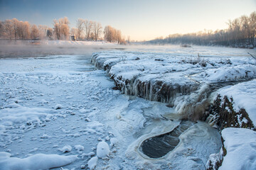 Frosty Venta river waterfall, the widest waterfall in Europe, in sunny, foggy winter morning, Kuldiga, Latvia - obrazy, fototapety, plakaty