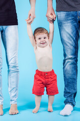 Family Ideas and Concepts. Lovely Caucasian Kid With Ppositive Facial Expression Hanging on Parental Hands Standing Together Against Blue Background.