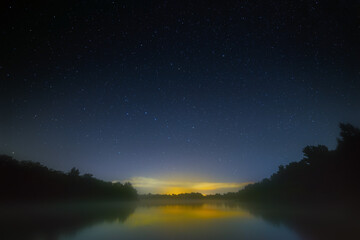 Night sky with bright stars over the river with fog. Summer landscape in Russia.