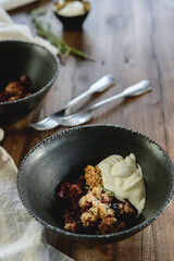 Homemade plum crumble pie with whipped cream in bowl on wooden table. Selective focus