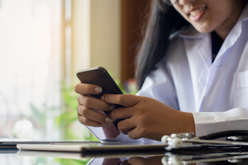 Young female doctor or medical student using mobile smart phone with digital tablet and stethoscope on the desk at office in clinic or hospital.