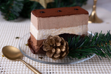 Obraz na płótnie Canvas A piece of cake or chocolate pie or souffle decorated with pine cone branches of a Christmas tree on a light background. New year gifts, festive and festive concept.
