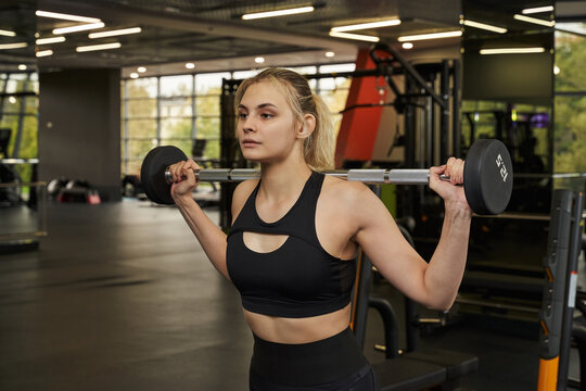 young woman in the gym holding a barbell on her shoulders